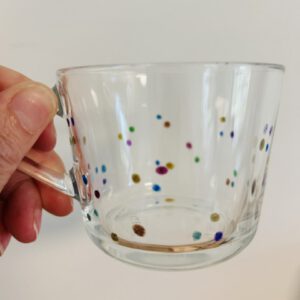 Glazen theekop met kleine gekleurde stippen, vastgehouden in een hand