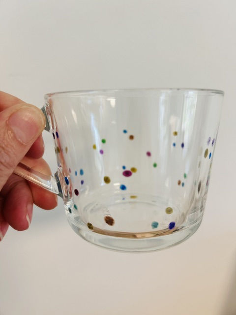 Glazen theekop met kleine gekleurde stippen, vastgehouden in een hand